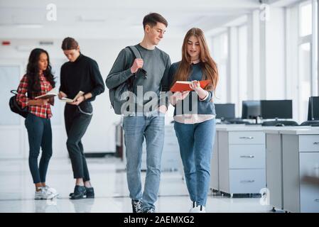 La lecture de l'information de livre avec couvercle rouge. Groupe de jeunes marchant dans le bureau à leur pause Banque D'Images