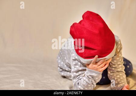 Célébrations de Noël épuisante - enfant de quatre ans avec une fille rouge Santa hat étant épuisés gisant sur le sol et repose sa tête sur son han Banque D'Images