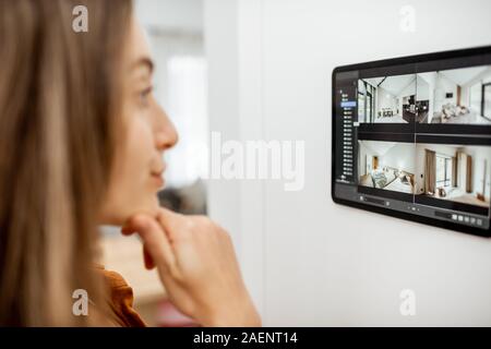 Jeune femme regardant la vidéo à partir de caméras de sécurité sur une tablette numérique à la maison. Concept de vidéo surveillance à distance via internet avec des appareils intelligents Banque D'Images