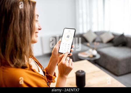 Young woman holding smart phone avec l'application de sécurité lancé à la maison. Concept de contrôle et la gestion de la sécurité à la maison à partir d'un terminal mobile Banque D'Images