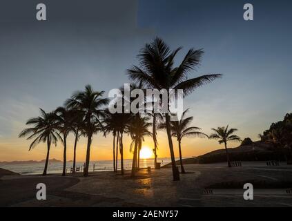 Lever du soleil sur le boulevard avec les démons de l'Arpoador beach et la silhouette des palmiers à Rio de Janeiro contre un ciel bleu clair et orange Banque D'Images