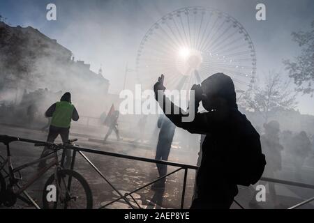 Lyon, France. Dec 10, 2019. Un manifestant lui-même des films dans la brume des gaz lacrymogènes et des pièces pyrotechniques, lors d'une manifestation dans le cadre de grèves et manifestations contre la réforme des retraites en France à la place Bellecour. La grève générale et des manifestations violentes à Lyon également conserver les fans de l'équipe de football Bundesliga RB Leipzig sur leurs orteils. À midi, le mardi, le club a mis en garde ses partisans de ne pas répondre à la Place Bellecour pour un entraînement commun pour le stade. Peu de temps après, il y a eu des affrontements entre manifestants et policiers sur et autour de la place. Photo : afp photo/Alamy L alliance Banque D'Images