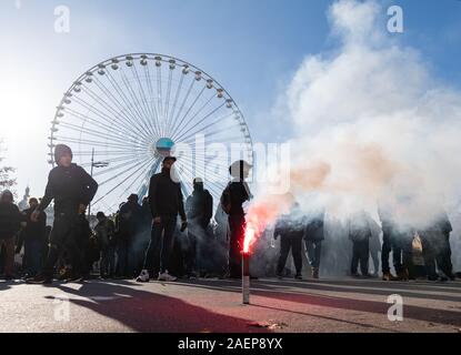 Lyon, France. Dec 10, 2019. La Pyrotechnie burns lors d'une manifestation dans le cadre de grèves et manifestations contre la réforme des retraites en France à la place Bellecour. La grève générale et des manifestations violentes à Lyon également conserver les fans de l'équipe de football Bundesliga RB Leipzig sur leurs orteils. À midi, le mardi, le club a mis en garde ses partisans de ne pas répondre à la Place Bellecour pour un entraînement commun pour le stade. Peu de temps après, il y a eu des affrontements entre manifestants et policiers sur et autour de la place. Les canons à eau et des gaz lacrymogènes ont été utilisés, les hélicoptères de l'encerclé paysage. Credit : dpa Banque D'Images