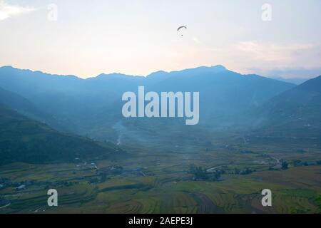 Le parapente survole les champs de terrasses de riz vert, brun, jaune et doré de la vallée de Tu le, au nord-ouest du Vietnam Banque D'Images