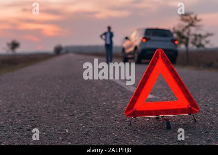 Triangle d'avertissement panneau sur la route, en arrière-plan flou femme appelant à l'assistance routière par la rupture de la voiture, selective focus Banque D'Images