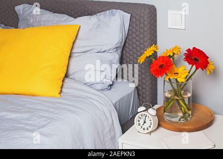 L'intérieur de chambre à coucher avec un coussin déco sur le lit et fleurs disponible sur la table de chevet. Banque D'Images