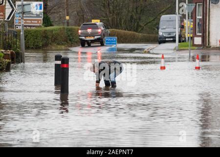 Aberfoyle, Stirlingshire, Scotland, UK. Dec 10, 2019. Royaume-uni - un homme tient un clair de vidange sur la rue principale à Aberfoyle durant une journée de fortes inondations après la rivière Forth éclate ses banques Credit : Kay Roxby/Alamy Live News Banque D'Images