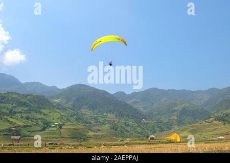 Le parapente survole les champs de terrasses de riz vert, brun, jaune et doré de la vallée du Tu le, nord-ouest du Vietnam Banque D'Images