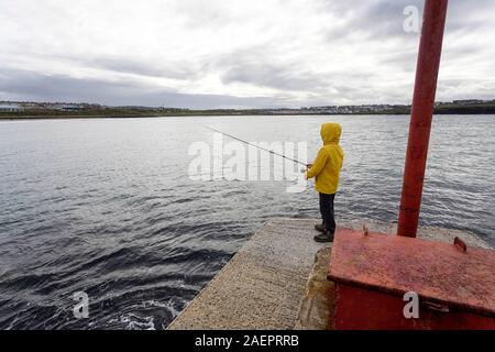 Jeune garçon en veste jaune à la pêche dans l'Arbour, Portrush, comté d'Antrim, l'Ulster (Irlande du Nord, l'Europe Banque D'Images