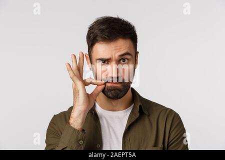 Mes lèvres sont scellées avec promesse. Sérieux et drôle adultes barbu homme garder bouche fermée, ce geste zip et soulever un sourcil en laissant personne séjour Banque D'Images