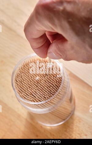 Mans part prendre un cure-dent en bois hors d'un récipient en plastique transparent debout sur une table en bois Banque D'Images