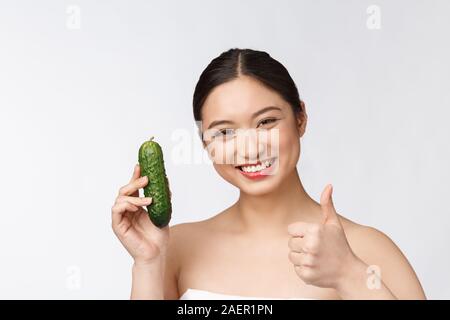 Jeune femme asiatique sur fond isolé tenant le concombre. Banque D'Images