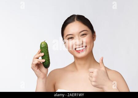 Jeune femme asiatique sur fond isolé tenant le concombre. Banque D'Images