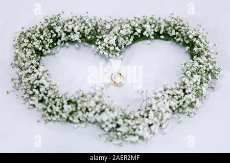 Arrangement de fleurs blanches en forme de coeur avec les anneaux de mariage attachés en ruban vert Banque D'Images