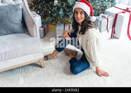 Femme dans un chapeau de Noël assis sur le tapis Banque D'Images