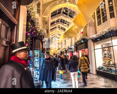 BURLINGTON ARCADE CHRISTMAS LONDON BEALES TOP HAT POLICE DE SÉCURITÉ PRIVÉE ET FENÊTRE DE FÊTE AFFICHER NOËL SHOPPING SHOPPERS INTÉRIEUR charmant olde worlde Burlington Arcade dans sa 200e année à Piccadilly avec des décorations de Noël traditionnelles lumières étincelantes et des foules de shoppers dans un milieu de shopping haut de gamme Londres Royaume-Uni Banque D'Images