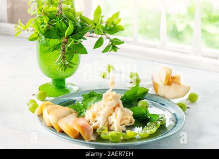 Soft blanc traditionnel fromage Cecil fibreux se trouve sur une plaque bleue. Le fromage est décorée de groseilles mûres et douce poire juteuse. Copier l'espace. Banque D'Images