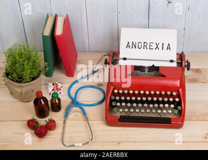 Trouble de l'alimentation concept - machine à écrire du texte avec l'Anorexie, blue stethoscope, pilules, machine à écrire rouge, fraises sur table en bois Banque D'Images