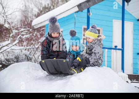 Heureux les enfants en luge en hiver en cour. Trois petits enfants dans des salopettes de jouer à l'extérieur sur journée d'hiver glacial. Trois frères chiens de petite sn Banque D'Images