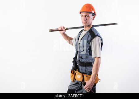 Un constructeur avec une grande épée sur son épaule. Réparateur portant un casque et des vêtements de travail. Banque D'Images