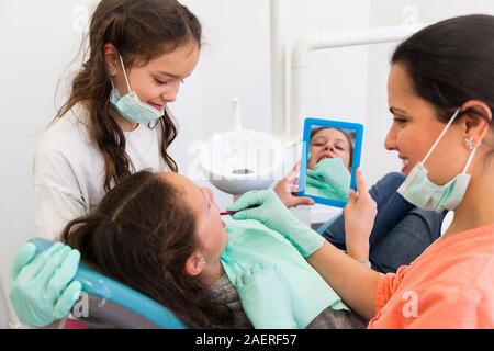 Deux enfants d'une femme agréable avec la chirurgie dentaire dentiste leur montrant comment brosser les dents Banque D'Images