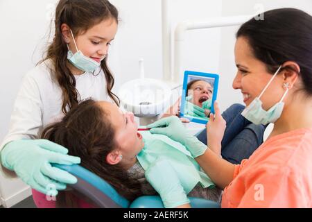 Deux enfants d'une femme agréable avec la chirurgie dentaire dentiste leur montrant comment brosser les dents Banque D'Images