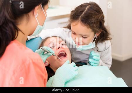 Adorables enfants dentiste en chirurgie dentaire avec deux jolies jeunes filles en leur montrant examen dentaire, une fille est à l'assistant Banque D'Images