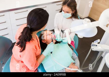 Adorables enfants dentiste en chirurgie dentaire avec deux jolies jeunes filles en leur montrant examen dentaire, une fille est à l'assistant Banque D'Images