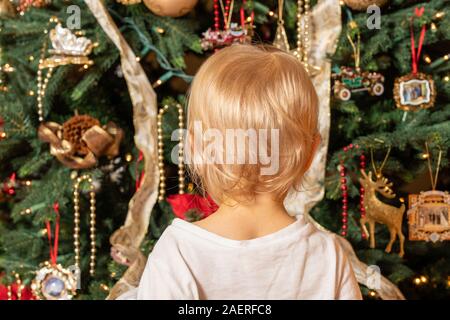 Vue arrière d'un young caucasian baby boy à regarder la magie d'un arbre de Noël pour la première fois dans l'émerveillement Banque D'Images