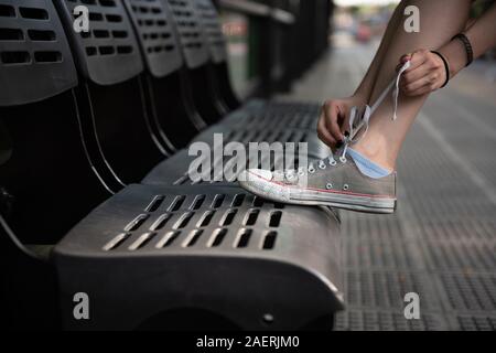 Une fille lui attacher ses lacets tout est en attente de l'autobus Banque D'Images