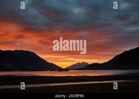 Un spectaculaire coucher de soleil sur le Loch Leven au cours d'une soirée d'automne avec les couleurs des nuages se reflétant dans l'eau et les montagnes en silhouette Banque D'Images