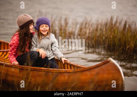 Deux sœurs parler et rire comme ils sont assis ensemble dans un canot en bois entre les roseaux roseaux sur un lac. Banque D'Images