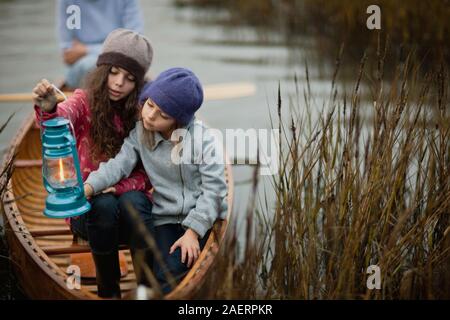 Jeune fille est titulaire d'une lanterne allumée et la montre à sa jeune sœur, assis ensemble à la proue d'un canot en bois entre les roseaux sur la rive d'un lac. Banque D'Images