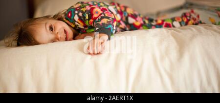 Smiling girl lying on bed en pyjama. Banque D'Images