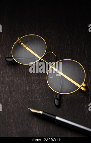 Lunettes d'or, la plume sur un fond de bois foncé.. Banque D'Images