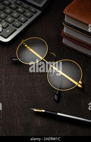 Lunettes d'or, calculatrice, bloc-notes, stylo sur un fond de bois sombre., Banque D'Images