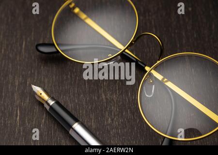 Lunettes d'or, la plume sur un fond de bois foncé.. Banque D'Images