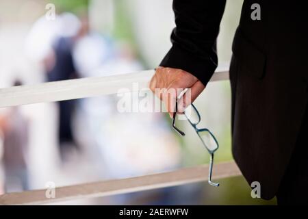 Businesswoman holding une paire de lunettes dans sa main se dresse sur un balcon. Banque D'Images