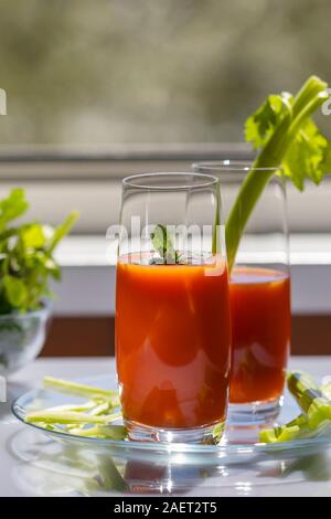 Jus de tomate avec le céleri sur un tableau blanc près de la fenêtre. Banque D'Images