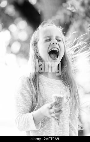 La crème glacée la fait tomber dans l'euphorie. Cute little girl eating ice cream on journée d'été. Petit enfant de lécher la crème glacée à l'extérieur du cône. Adorable happy kid appréciation des crème glacée dessert. Banque D'Images