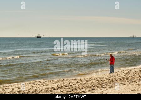 L'homme la pêche dans le golfe du Mexique sur Dauphin Island avec bateaux de crevettes à l'arrière-plan, sur l'Île Dauphin Alabama, Etats-Unis. Banque D'Images