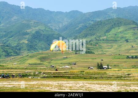 Le parapente survole les champs de terrasses de riz vert, brun, jaune et doré de la vallée du Tu le, nord-ouest du Vietnam Banque D'Images