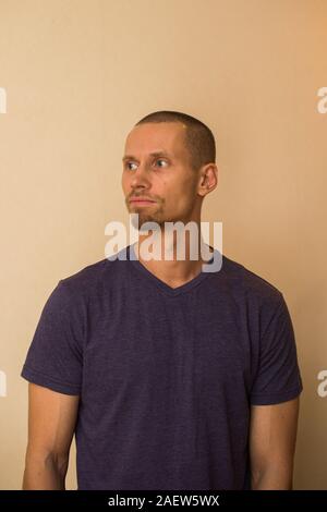 Un beau jeune homme dans un tee-shirt bleu pose contre un mur beige Banque D'Images
