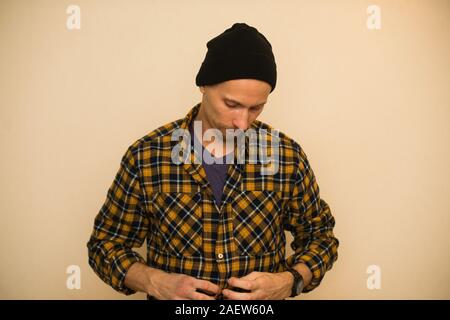 Jeune homme, modèle de la mode, portant une chemise à carreaux avec un aveugle beige derrière lui. Guy in black hat avec barbe en style casual Banque D'Images