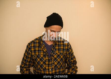 Jeune homme, modèle de la mode, portant une chemise à carreaux avec un aveugle beige derrière lui. Guy in black hat avec barbe en style casual Banque D'Images