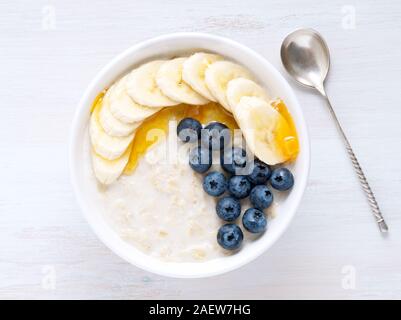 Avoine avec bananes, myrtilles, Chia, confiture, miel, sur un fond de bois blanc. Petit déjeuner sain. Vue d'en haut Banque D'Images