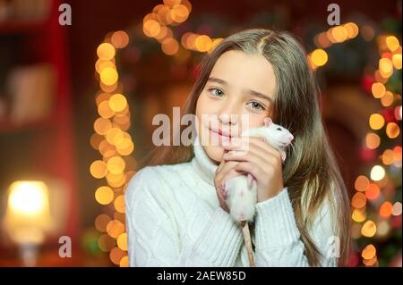 Cute little girl tient dans ses bras et l'étreignant un rat blanc drôle sur fond de lumières de Noël lumineux. Symbole de 2020. Animaux domestiques Banque D'Images
