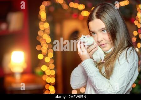 Cute little girl tient dans ses bras et l'étreignant un rat blanc drôle sur fond de lumières de Noël lumineux. Symbole de 2020. Animaux domestiques Banque D'Images