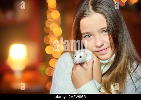 Cute little girl tient dans ses bras et l'étreignant un rat blanc drôle sur fond de lumières de Noël lumineux. Symbole de 2020. Animaux domestiques Banque D'Images