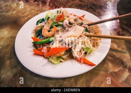 Pad Thaï de fruits de mer plat de nouilles de riz frit thaïlandais sur une plaque blanche avec des baguettes et de carotte râpée garniture. Banque D'Images